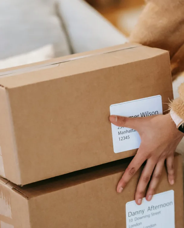 Stacked shipping boxes with mailing labels and a hand checking a package, for Selfnamed wholesale retailers