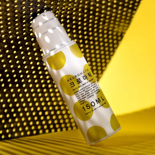 Cosmetic bottle wrapped in a yellow polka-dot pattern, dramatically lit against a dark background.