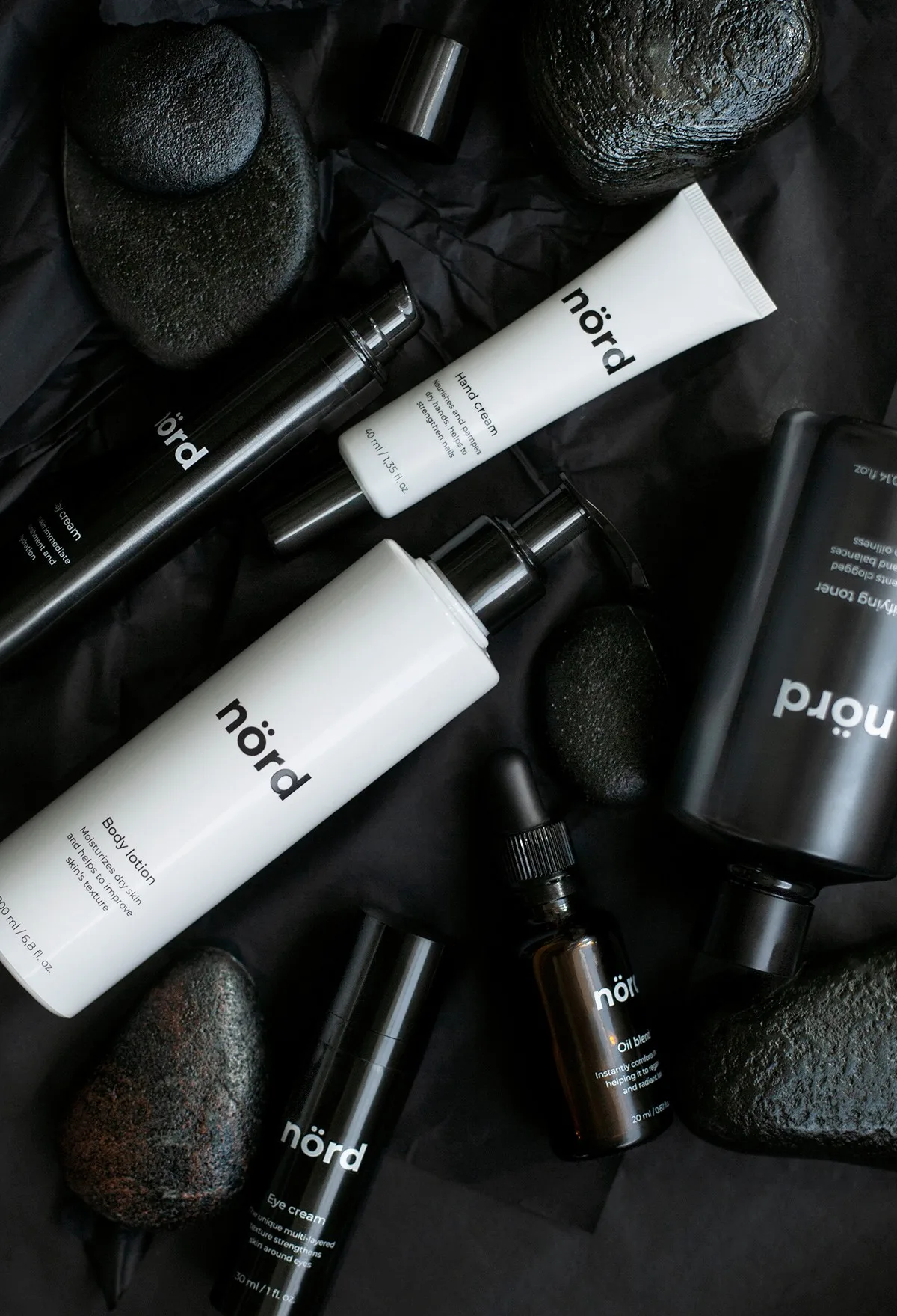 Flat lay of Nörd-branded skincare bottles and tubes on dark stones.
