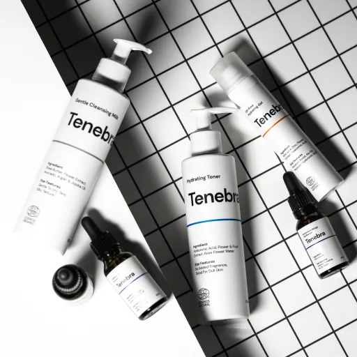 Skincare bottles and tubes from the Tenebra product line arranged on a grid-patterned background.