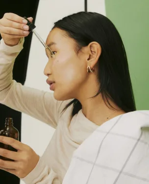 Woman applying facial serum with a dropper while filming content.