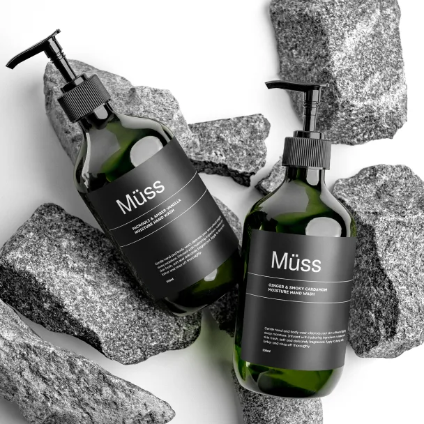 Two dark green Müss pump bottles standing among grey stones.